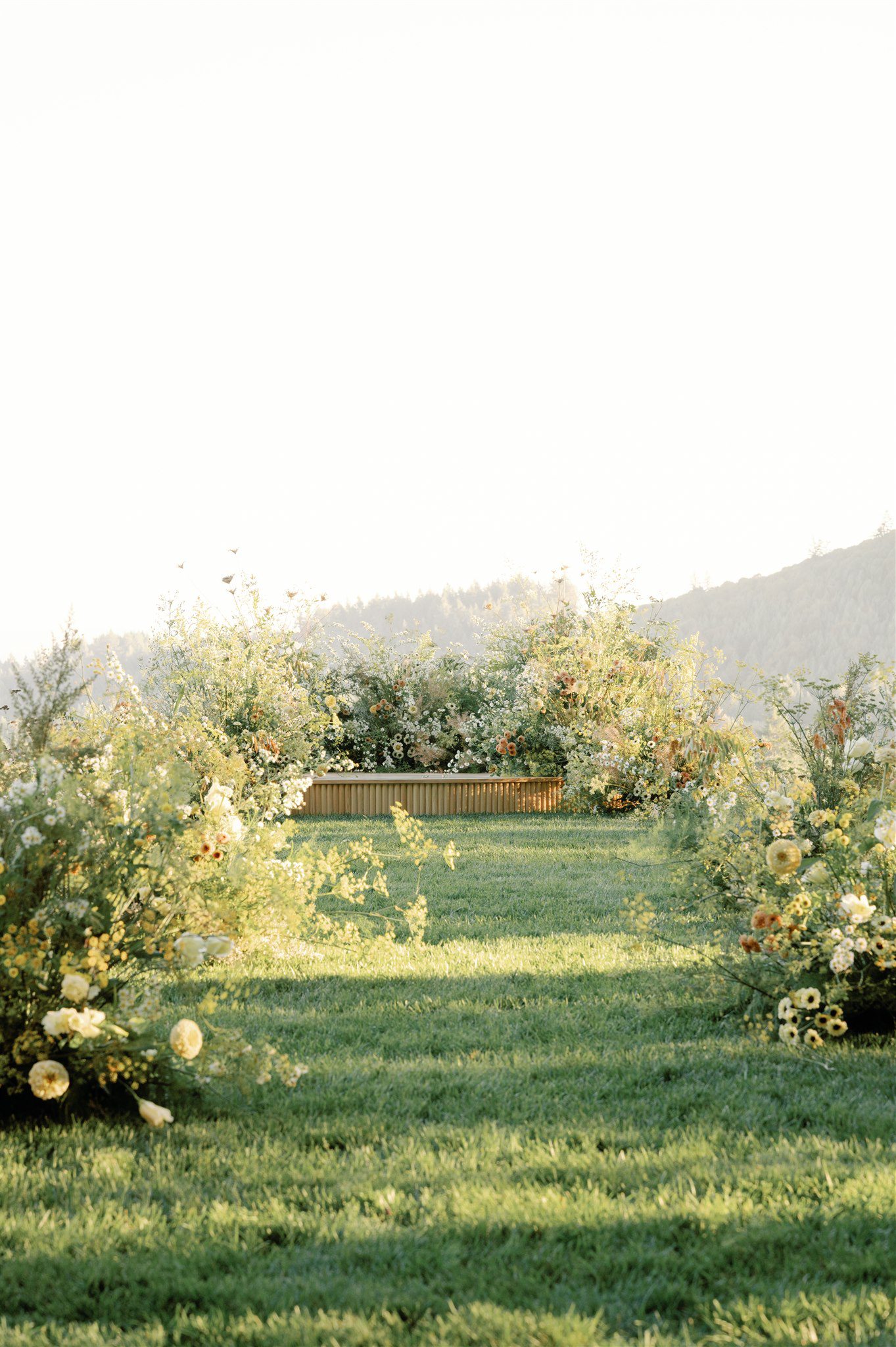 Wedding ceremony built from wildflowers and greenery framing a vineyard hillside backdrop.