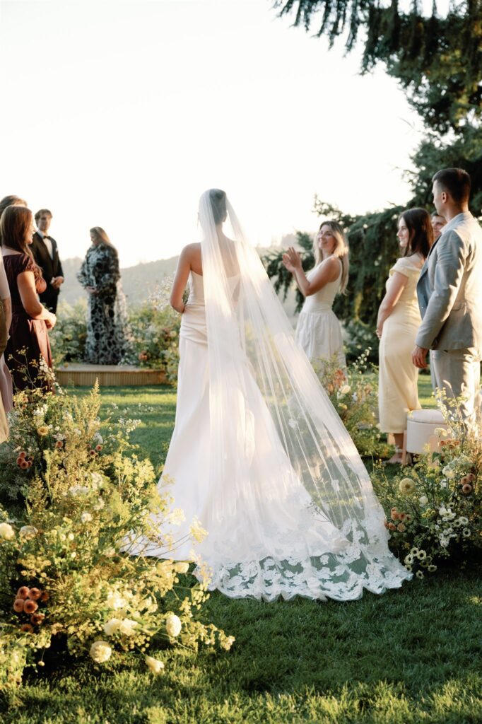 Bride walking through a wildflower-lined ceremony aisle at a wine country destination wedding.